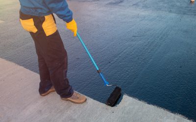 Worker applies bitumen mastic on the foundation Roofer worker painting black coal tar or bitumen at concrete surface by the roller brush, A waterproofing. industrial worker on construction site laying sealant for waterproofing cement